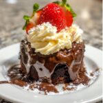 Chocolate lava cake topped with whipped cream and a strawberry, served on a white plate with melted chocolate oozing out.
